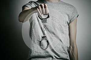 Prison and convicted topic: man with handcuffs on his hands in a gray T-shirt on a gray background in the studio, put handcuffs on photo