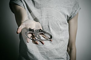 Prison and convicted topic: man with handcuffs on his hands in a gray T-shirt on a gray background in the studio, put handcuffs on photo
