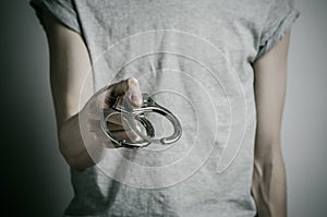 Prison and convicted topic: man with handcuffs on his hands in a gray T-shirt on a gray background in the studio, put handcuffs on