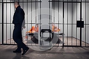 A prison guard with a baton makes a tour of the prison cells before lights out. Two prisoners in red robes are behind