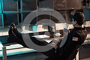 prison guard sitting with legs on table and monitoring people