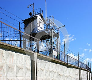 A prison tower with a concrete fence and barbed wire