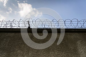 Prison wall barbed wire fence with blue sky in background