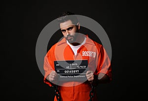 Prisoner with chained hands holding mugshot letter board on black background