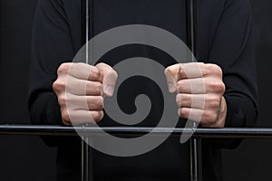 Prisoner holding hands in fists on courtroom bars, dark tone, selective focus.
