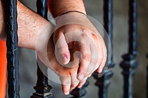 Prisoner man holding hands on jail bars. Hands on prison bars