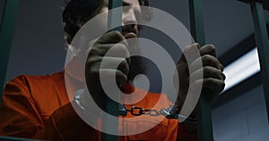 Prisoner in orange uniform and handcuffs holds metal bars