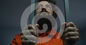 Prisoner in orange uniform and handcuffs holds metal bars