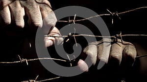 Prisoner`s hands shake the rusty barbed wire in the darkness lit by hard light. 4K video.