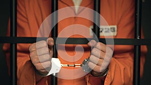 Prisoner showing hands in handcuffs, dangerous criminal standing behind bars