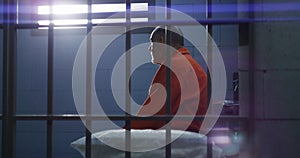 Prisoner sits on bed and looks on barred window