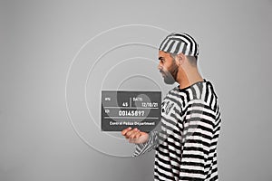 Prisoner in special uniform with mugshot letter board on grey background, space for text