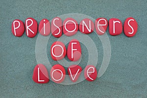 Prisoners of love, negative thoughts composed with red colored stone letters over green sand