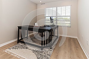Pristinely clean, empty room with a desk situated in the corner, and natural light from the windows photo