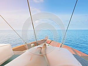 Private boat trip on open sea. Image shows legs of a woman lying on a thick and comfortable cushion laid on top of boat.