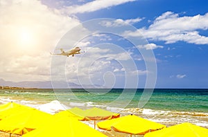 Private business plane on landing flies over sandy beach with sun loungers on background of sunset, sun and clouds