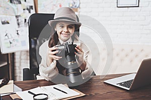 Private detective agency. Little girl is sitting at desk looking at photos in camera.