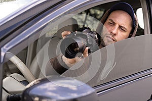 Private detective with camera spying from car, taking photo with professional camera