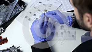 Private detective checking fingerprints on bullet using tweezers, investigation