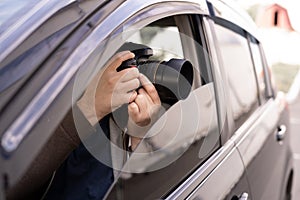 Private detective or investigator or paparazzi taking photos on street while sitting in car