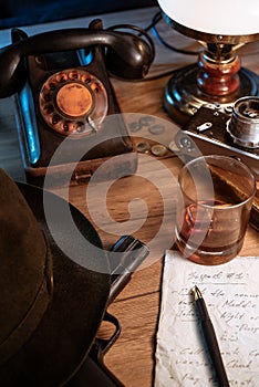 Private detective`s desk, noir still life with a vintage phone, typewriter, lamp, gun and retro photos