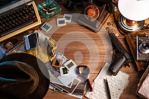 Private detective`s desk, noir still life with a vintage phone, typewriter, lamp, gun and retro photos