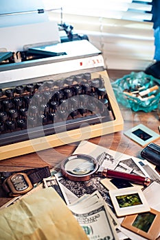 Private detective`s desk, noir still life with a vintage phone, typewriter, lamp, gun and retro photos