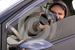 private detective sitting inside car taking picture with professional slr camera