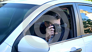 Private detective spying from car, taking photos on camera, investigation