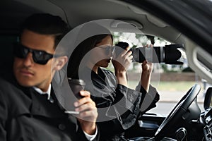 Private detectives with modern camera spying from car photo