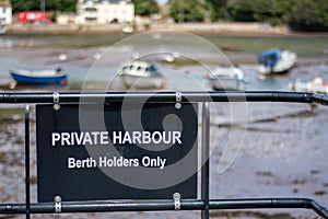 Private harbour berth holders only sign in black at a pretty harbor at low tide.