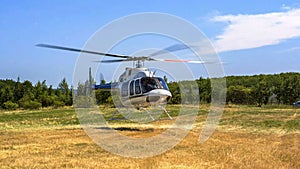 Private helicopter taking off in the middle of a meadow with green grass and forests