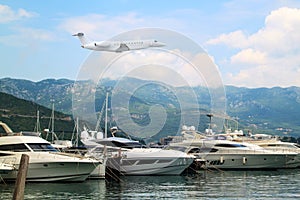 Private jet business plane flies low over yachts and boats in gulf of  background of mountains with white clouds