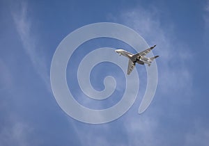 Private jet with landing gear down flying across blue sky with white cirrus clouds.ar sunset