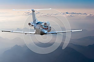 Private jet, passenger wide-body plane or aircraft is flying in the blue sky over the the clouds and mountains. Summer