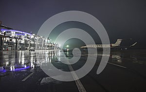 A private jet white business jet stands in the airport parking lot at night against the backdrop of a glowing airport terminal at