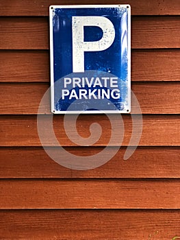 Private parking sign on wooden wall. Blue sign and white color text `Private parking`