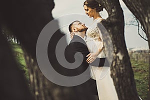 Private photo peeping from behind the bride and groom from the trees. Amorous couple on a natural background. In artistic creative