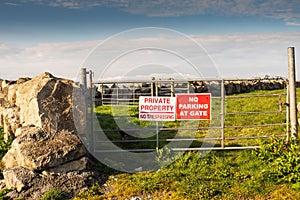 Private property no trespassing and no parking at gate signs on a metal gate. Entrance to a agriculture land. Stone fence and blue