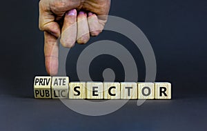 Private or public sector symbol. Businessman turns cubes and changes words `public sector` to `private sector`. Beautiful grey photo