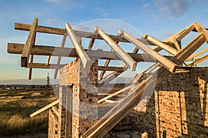 Private residential house with wooden roof frame structure under construction. Unfinished brick building under development