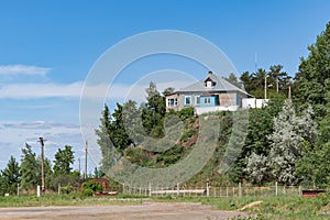 A private residential wooden house with an attic is built and is located on the mountain. Bushes and trees grow around the house