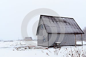 Private rustic two-storey house from the siding without a fence in a field in winter in the snow.