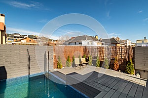 Private terrace on the roof of a house with swimming pool, sunbeds and wooden fence on sunny day in Barcelona.