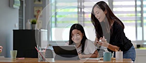 Private tutor teaching her student with digital tablet and stationery on wooden table in living room