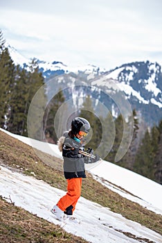 Problem of global warming and winter skiing. One Asian walking downhill with ski in hands. Climate change with disappearance of photo