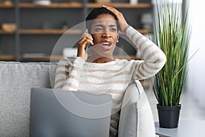 Problem With Internet. Confused Black Woman Talking On Cellphone And Using Laptop