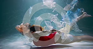 The problem of plastic. Young tourist woman swims under water surrounded by garbage waste floating around slow motion.