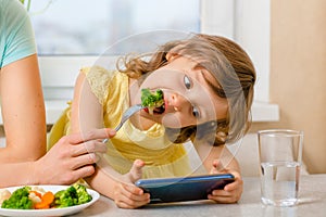 The problem is to distract the child from the phone and feed it with broccoli. A way to feed children