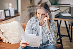 Young man in jeans shirt holding papers and looking troubled